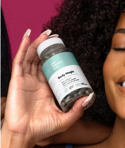 Woman holding a Her Fantasy Box Body Magic supplement bottle, smiling with eyes closed.